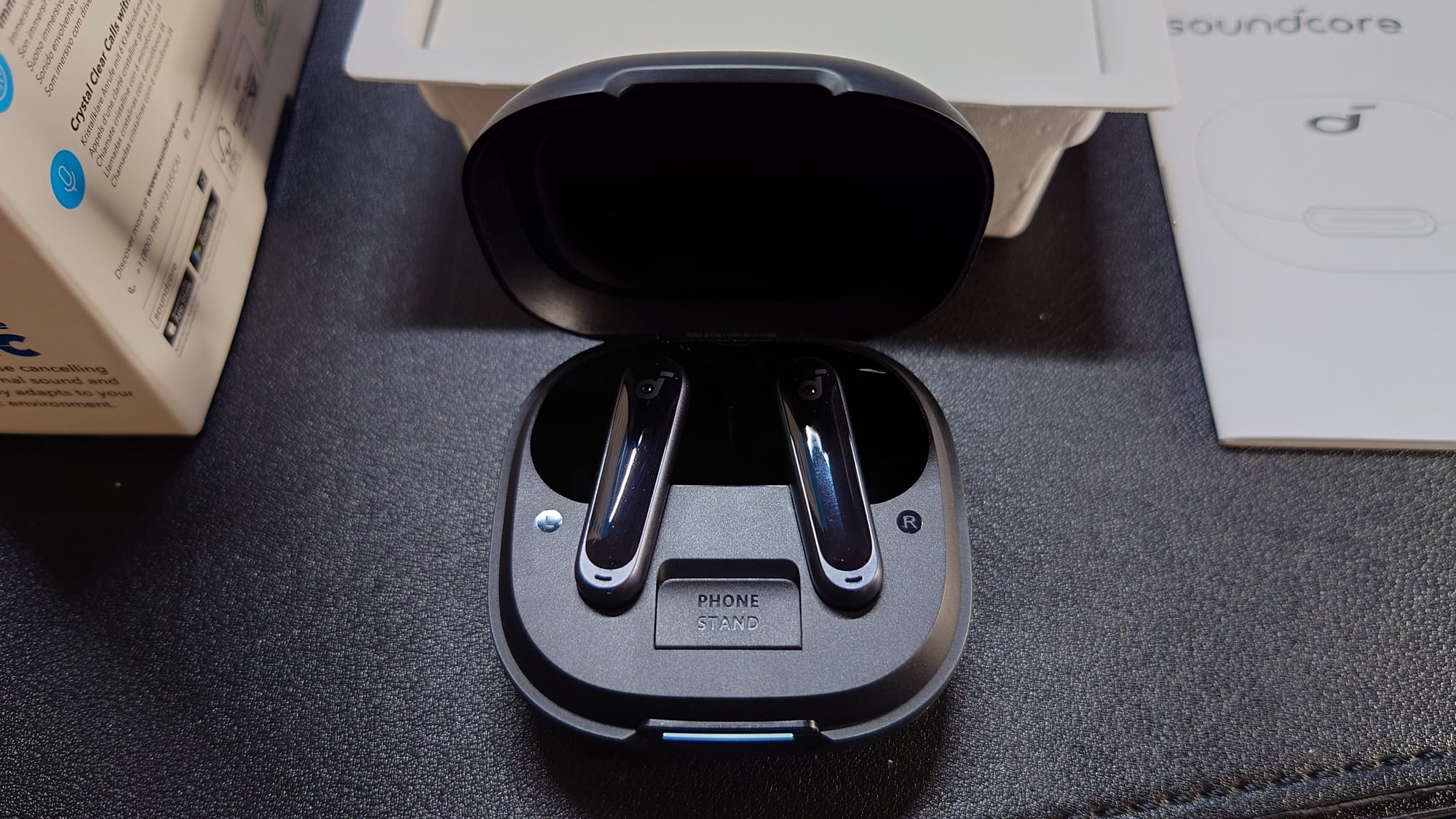 The Soundcore P40i are in their open case.  Beneath them can be seen the phone stand, which can be popped open to prop up a phone in landscape mode.