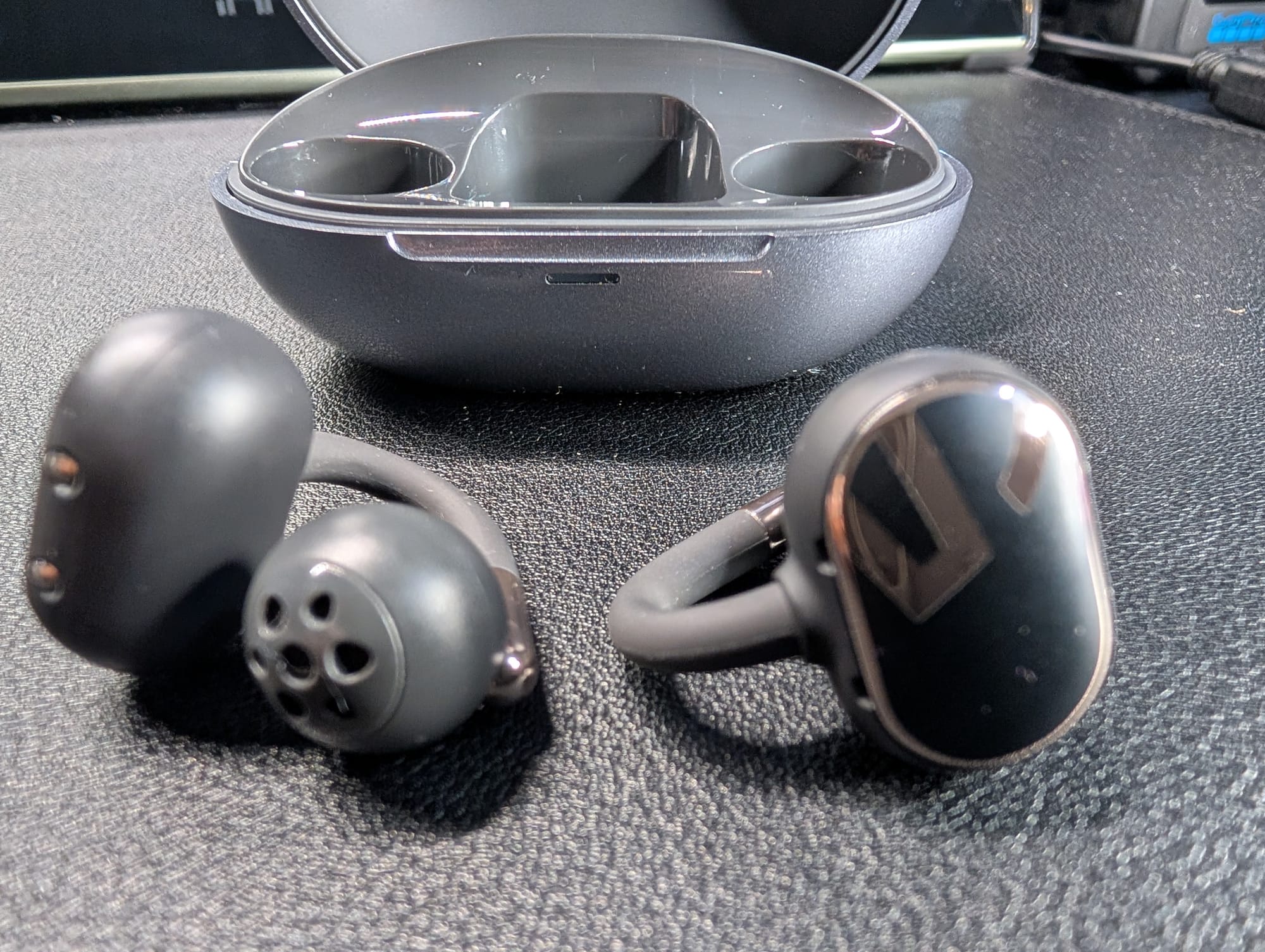 The SoundPeats Clip 1 outside their case; they are dark grey with gold accents and a gold S logo on the back plate