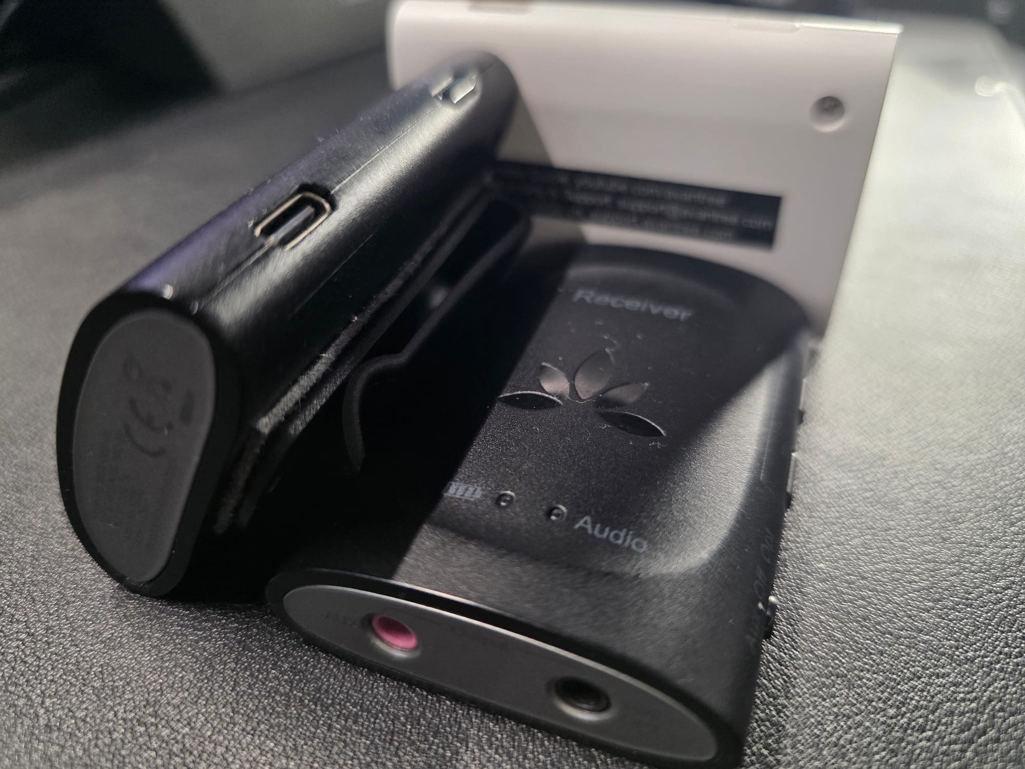 The Avantree kit lying on a black desk. One receiver is on its side and the other is on its back. The transmitter has its back side showing. The Avantree receivers are black and the transmitter is white.