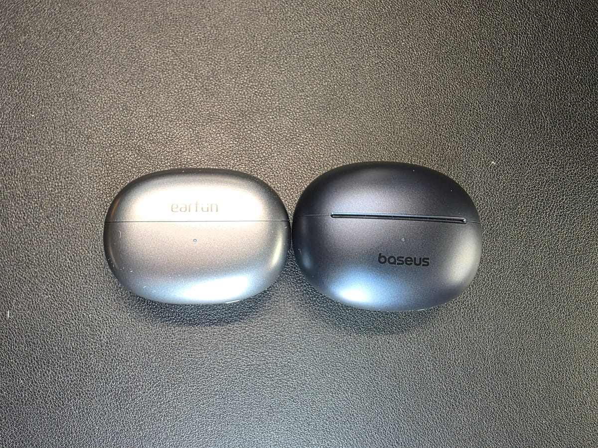 The EarFun Clip are shown in their closed gray case on the left and the Baseus Bowie MC1 Pro in its closed charcoal case on the right