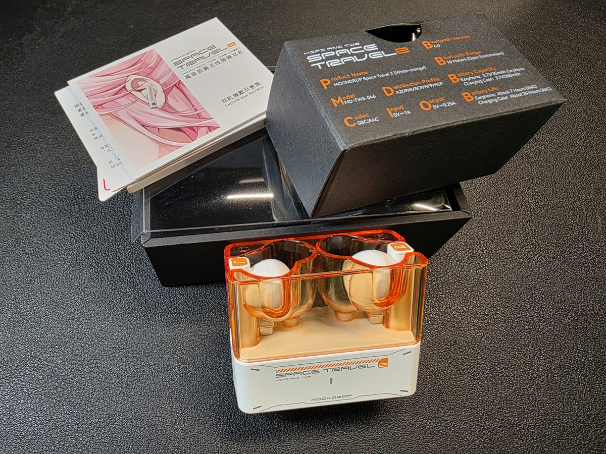 The Moondrop Space Travel 2 are pictured in white in their charging case and the paperwork and box of eartips and cable is shown in the background