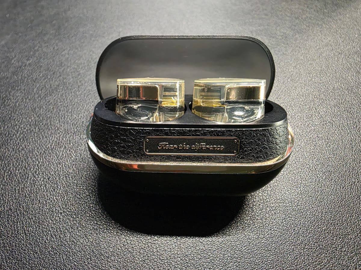SoundPeats open in their charging case. The case is black and the earphones are gold and transparent.