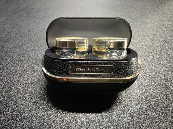 SoundPeats open in their charging case.  The case is black and the earphones are gold and transparent.